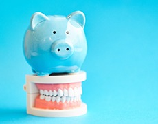 Cost of dental implants in New Bedford represented by piggy bank atop model teeth